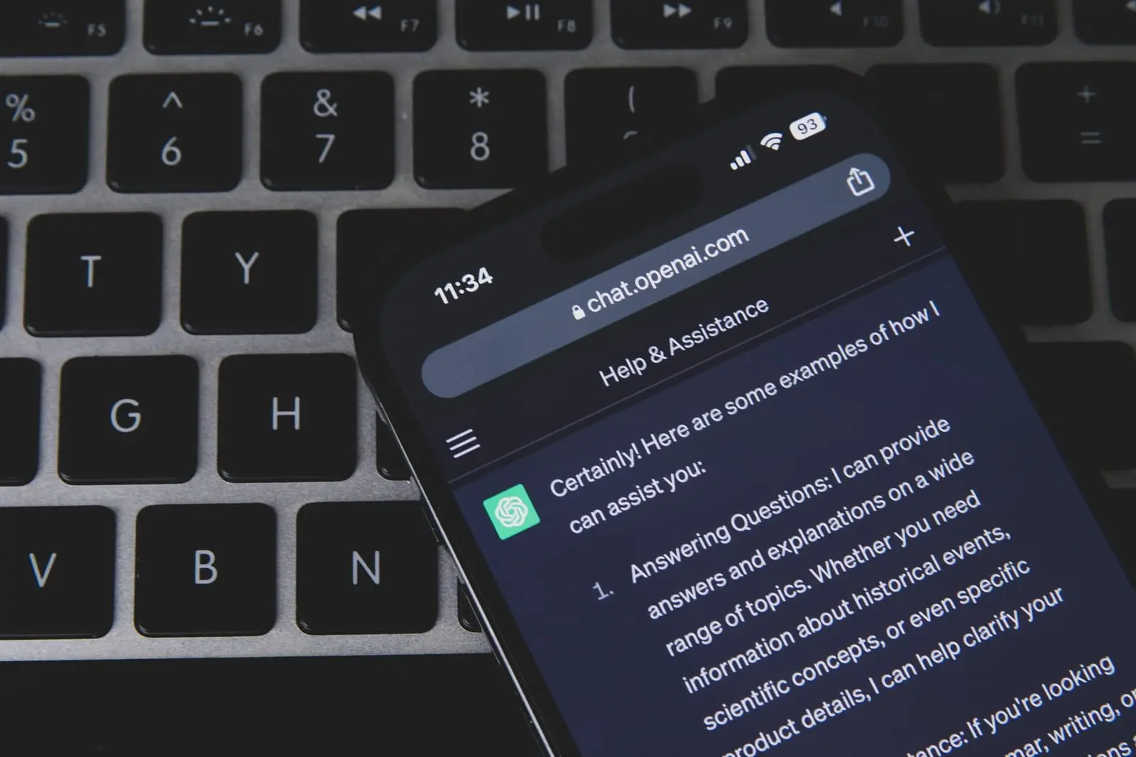 A smartphone showing the ChatGPT web app in a browser lies on a dark laptop keyboard.