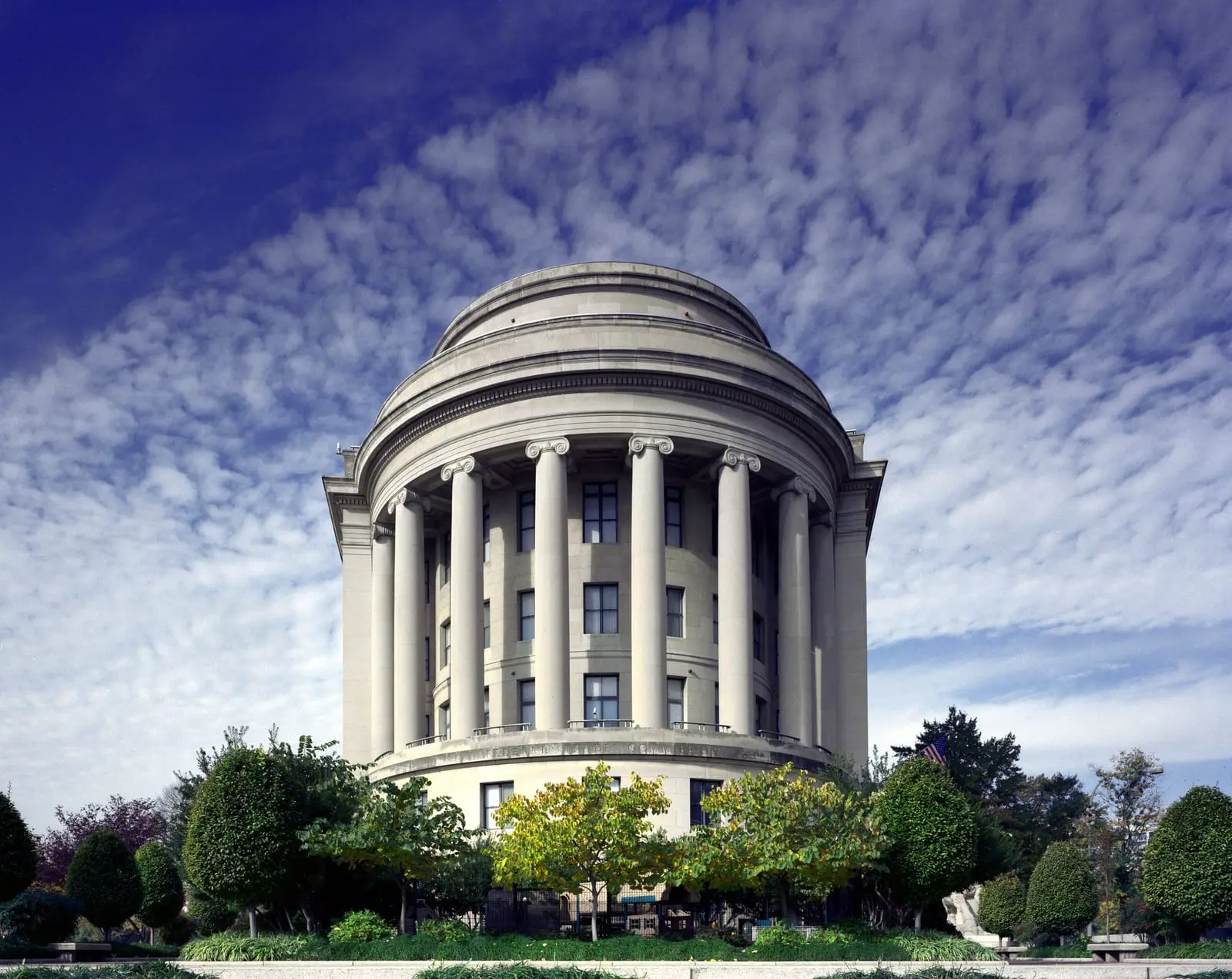 The rounded, colonnaded east end of the Federal Trade Commission building in Washington, DC, under a blue sky with scattered clouds.
