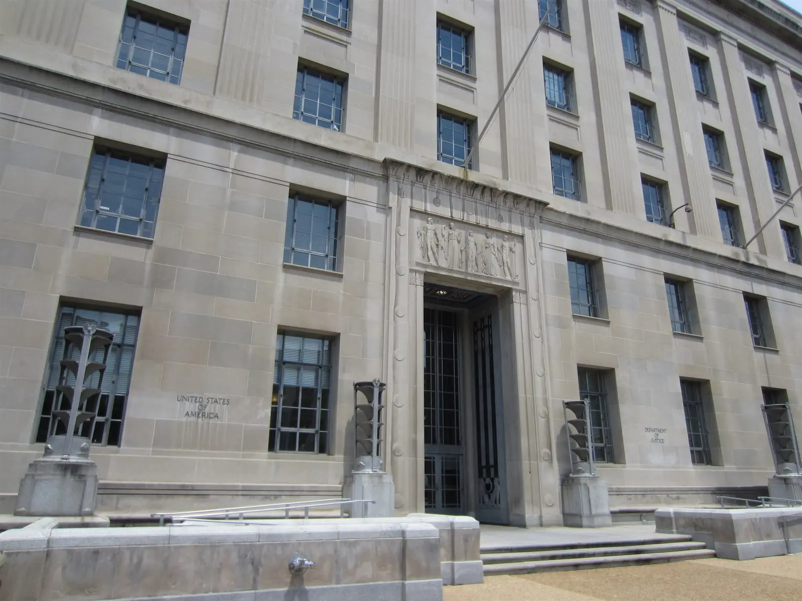 The stone facade and entrance of the US Department of Justice building in Washington, D.C., with tall windows and bronze lamp posts.