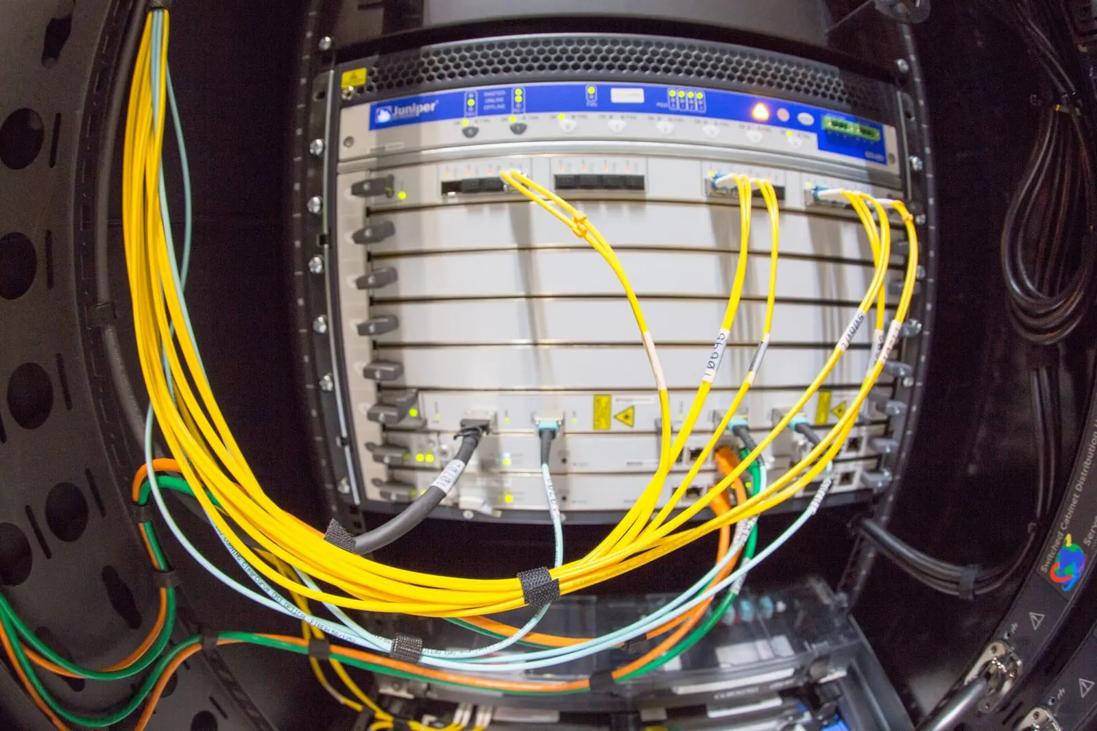 A network router in a server rack with bundles of yellow and blue fibre optic cables plugged into its ports.